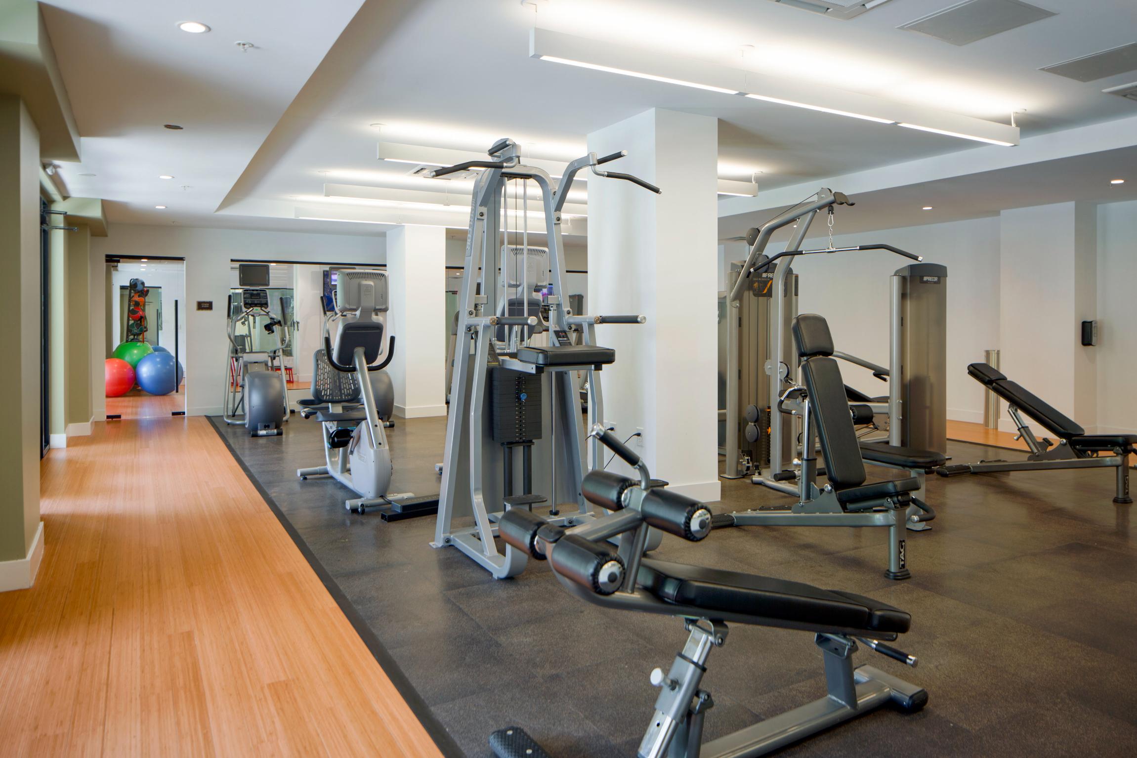 A gym with cardio and strength training equipment, with a mirrored wall and separate workout area.