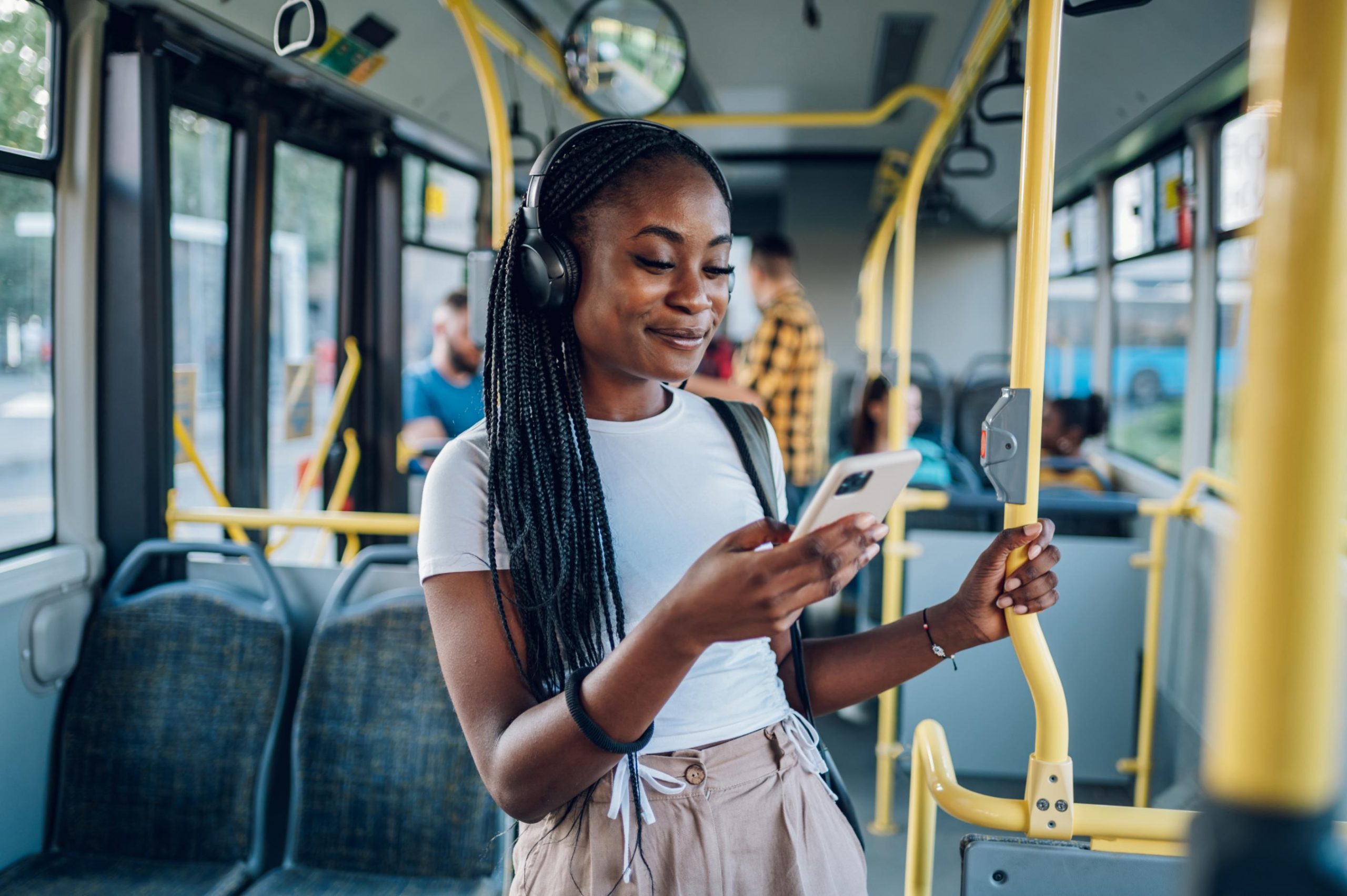 A young lady is looking at her phone and smiling while commuting on a bus.